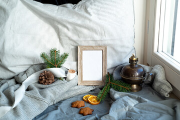 Cozy Christmas scene near the window. Winter interior. Blank wooden picture frame mockup. Wholemeal cookies, pillow, wool sweater,vintage wick oil lamp. Menu breakfast template