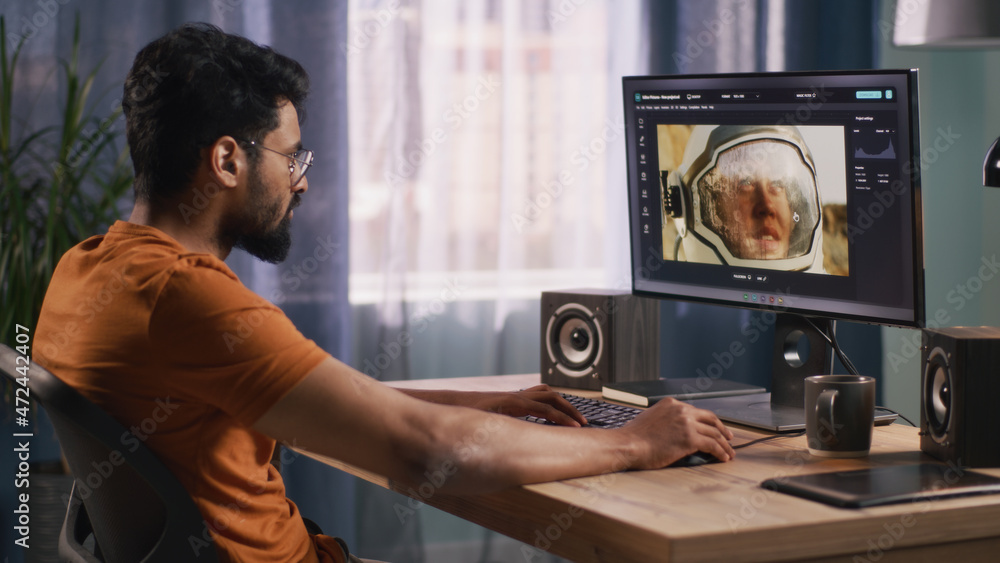 Poster side view of bearded indian man using retouching software on computer to edit picture of cosmonaut d