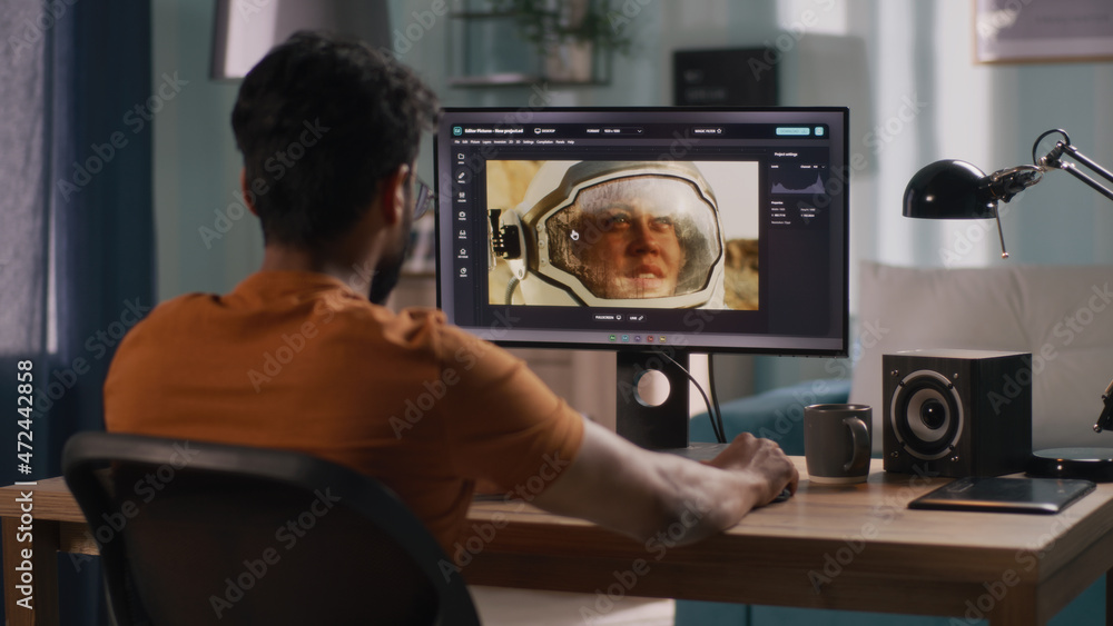 Poster back view of unrecognizable male retouching astronaut photo on computer while sitting at table and w