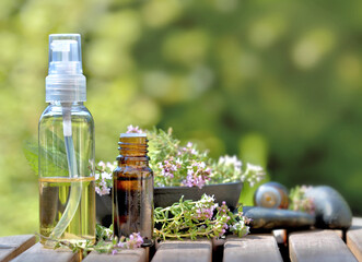 bottles of essential oil and flowers of aromatic herb on a table and on green background