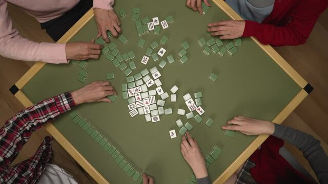 cropped shot with top view of four people's hands forming the wall of stacks with green white tiles on mahjong table while enjoying the indoor recreation at home on chinese new year