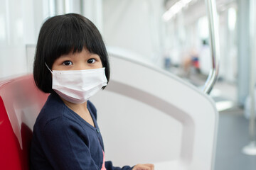 Fototapeta na wymiar Little girl with surgical mask face protection flu and Virus outbreak in public transportation (skytrain or subway). Concept of New normal lifestyle, Using public transport to travel to school.