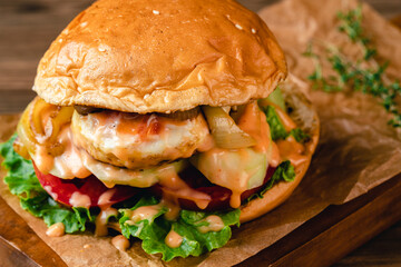 hamburger stuffed with fried egg, cucumber, tomato, mayonnaise, lettuce, onion on wood and dark background. 