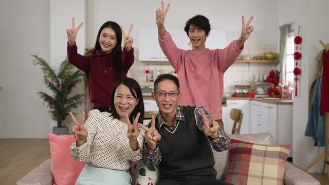 happy family of four smiling at camera with thumb and victory hand gestures while taking burst photos in a modern house interior with lunar new year decorations