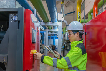 Asian engineer wearing glasses working in the boiler room,maintenance checking technical data of...