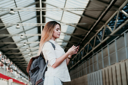 Young woman wearing backpack using smart phone at railroad station