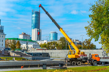 Mobile construction crane with yellow telescopic boom at the waterfront construction site in the city lifts a lever with a heavy load. © Евгений Панов