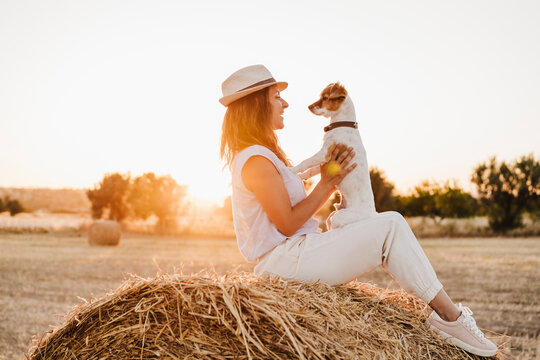 Woman wearing hat playing with dog on strawb bale