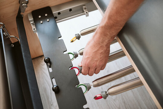 Man Adjusting Coiled Spring Of Pilates Machine In Studio