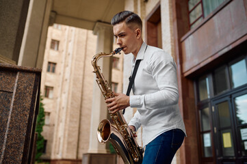 Male saxophonist plays the saxophone on the street - obrazy, fototapety, plakaty