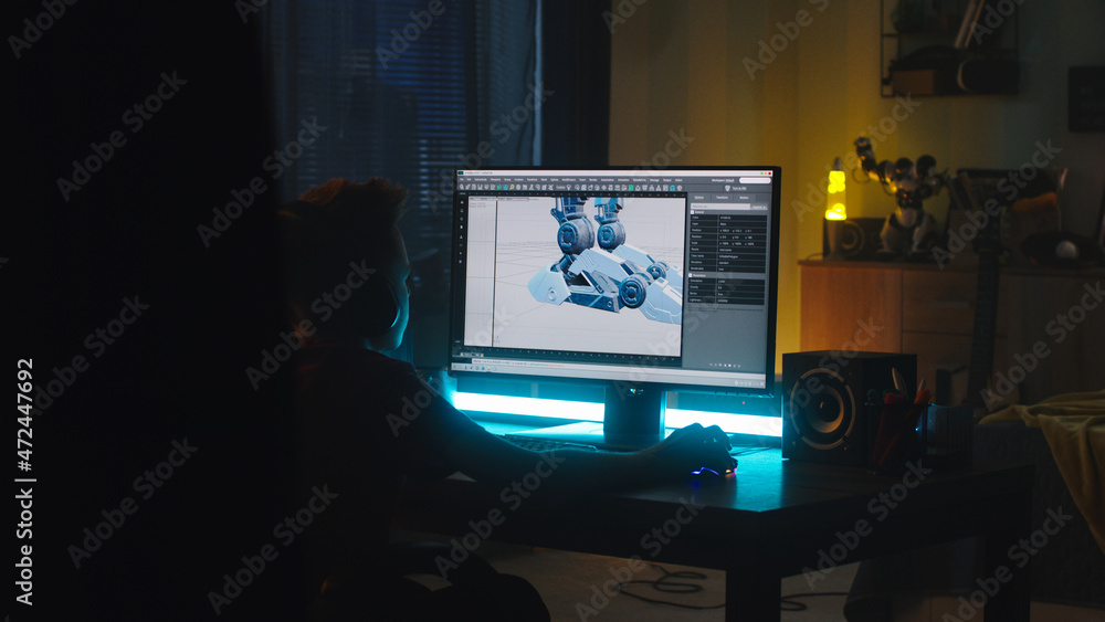 Poster anonymous teenager in headphones making 3d model of robot on computer while creating cartoon at nigh