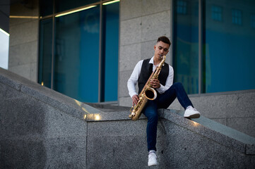 Male saxophonist poses at the stairs on street