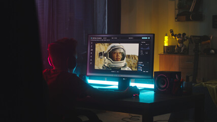 Male teenager using computer to retouch picture of astronaut while sitting at table and learning to use editing software at night at home