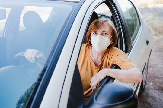Senior woman with protective face mask sitting in car during COVID-19