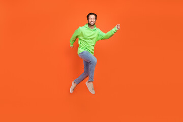 Fototapeta na wymiar Full body photo of brunet young guy run wear sweatshirt jeans sneakers isolated on orange background