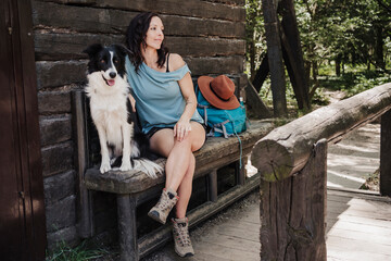Female tourist sitting with pet dog on bench by cottage in forest