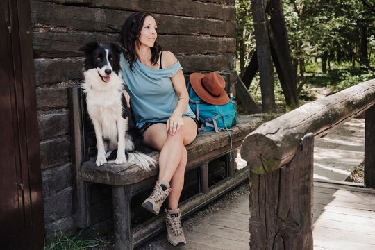 Female tourist sitting with pet dog on bench by cottage in forest