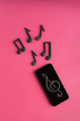 Smartphone, treble clef and musical note on pink background. Music apps. Music on your phone. Vertical frame