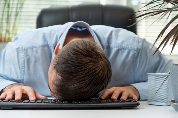 Young businessman working at computer, falling asleep in office on keyboard. Tired and fatigued office worker sleeping on desk.