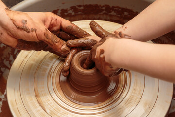The child moulds from clay a pot on a potter's wheel. Adults help the child to work with clay.