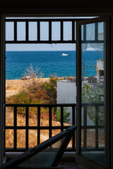 View through a broken window to the sea and the beach with palm trees on a sunny summer day. Poor life concept overlooking the rich
