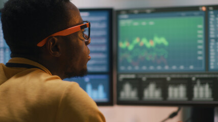 Rack focus of African American guy analyzing graphs and trading on stock market on computer in home office