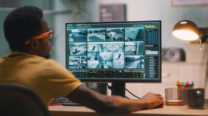 African American male security worker watching video from surveillance cameras on computer during...