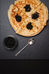 Russian cuisine dish - pancakes with black caviar on a slate plate, copy space