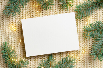 Christmas greeting card mockup with garland lights and fir tree branches on knitted background