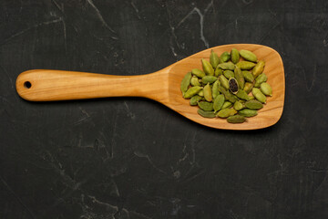 Wooden Spoon Full Of Spicy Indian Cardamom Pods, On A dark concrete Background. Flat lay