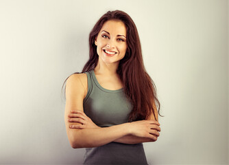 Obraz premium Beautiful casual cute toothy smiling woman hugging your self with folded strong arms in green t-shirt on vintage color background. Closeup portrait