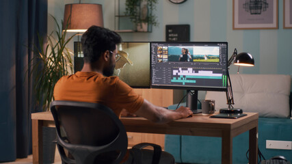 Unrecognizable man in orange t shirt using computer to edit video while sitting at table and...