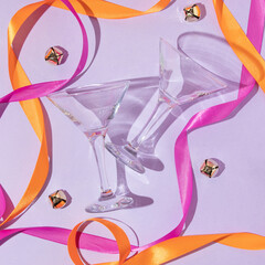 Obraz na płótnie Canvas New year creative layout with martini cocktail glasses, colorful satin ribbons and jingle bells on pastel purple background. 80s or 90s retro fashion aesthetic party concept. 
