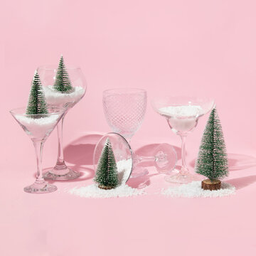 Christmas and New Year creative layout with christmas trees, snow and cocktail glasses on pastel pink background. Winter creative idea. 80s or 90s retro aesthetic party minimal concept.