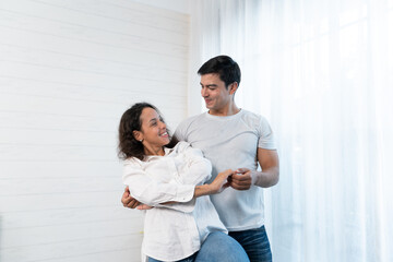 Happy Hispanic young couple having fun dancing in the bedroom, enjoying the dance on weekend at home