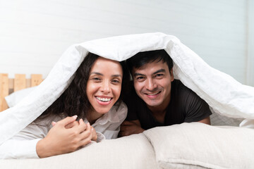 Happy Hispanic young couple lying down on the bed looking at the camera. concept of new relationship, dating, spending time together