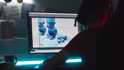 Anonymous teenager in headphones making 3D model of robot on computer while creating cartoon at...