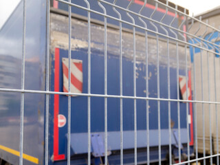 Defocused back view of a metal fence and part of a blue truck.