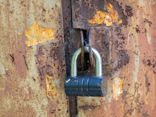 Aged damaged metal doors are padlocked. Rough rusty surface.