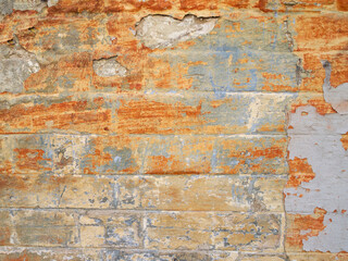 Side view of a colorful brick wall. Several layers of paint have peeled off and the surface is stained.