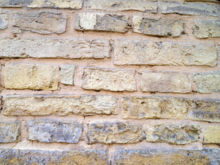 The wall is made of gray, beige and brown bricks. The damaged surface is covered with cracks and spots.