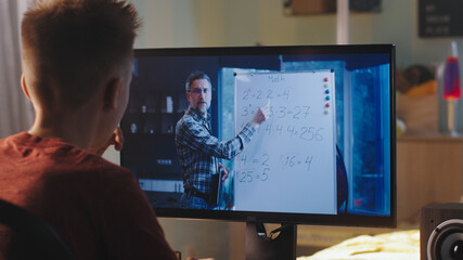 Back view of teen student listening and asking questions to math teacher during online lesson at home in daytime