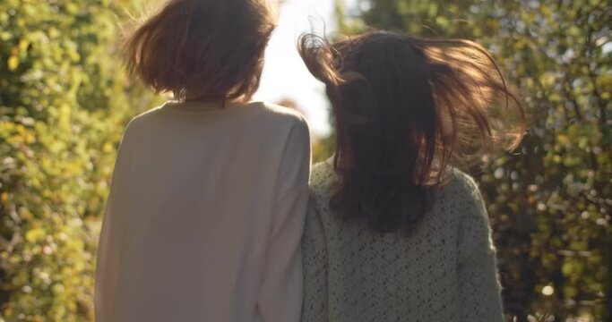 Young women walks together in slow motion in the sunsent light outdoors. Fashion stylish video of two girls in casual dree walking in the park, 4k 60p Prores HQ