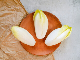 Top view of three raw fresh endives on a brown plate. Preparing for cooking.