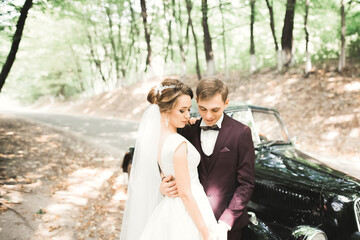 Stylish wedding couple, bride, groom kissing and hugging on retro car