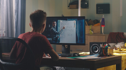 Back view of teen student listening and asking questions to math teacher during online lesson at home in daytime