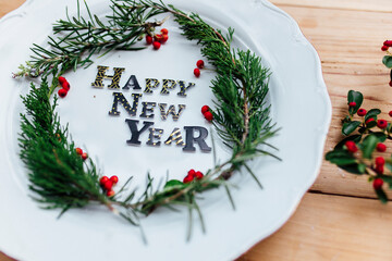 Happy New Year porcelain plate with Christmas wreath. Party decoration, flat lay, top view. Empty space. Restaurant menu concept. Isolated on wooden table background. Winter holidays background.