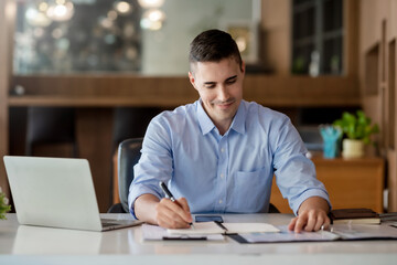 Obraz premium Businessman working on laptop and taking notes in office.