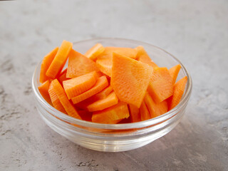 Side view of a transparent bowl with chopped carrots. Paysanne cut.