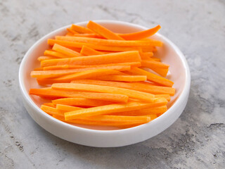 Pieces of raw chopped carrots in a white bowl on a gray background. Julienne carrot.